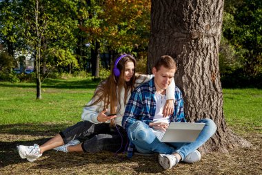 Genç bir çift, dizüstü bilgisayarı, kulaklığı ve telefonu olan bir ağacın yanında otururken parkta birlikte zaman geçirir, çalışır ve çalışır. Parkta aletleri olan bir kızla birlikte olan adam.