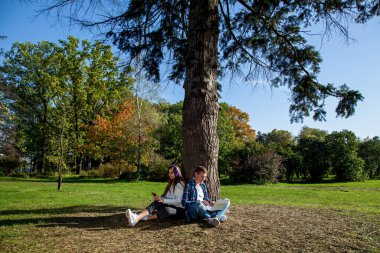 Genç bir çift, dizüstü bilgisayarı, kulaklığı ve telefonu olan bir ağacın yanında otururken parkta birlikte zaman geçirir, çalışır ve çalışır. Parkta aletleri olan bir kızla birlikte olan adam.
