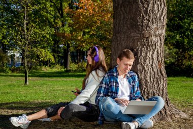 Genç bir çift, dizüstü bilgisayarı, kulaklığı ve telefonu olan bir ağacın yanında otururken parkta birlikte zaman geçirir, çalışır ve çalışır. Parkta aletleri olan bir kızla birlikte olan adam.
