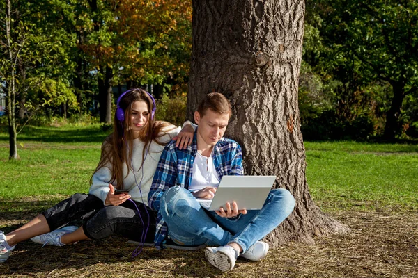 Genç bir çift, dizüstü bilgisayarı, kulaklığı ve telefonu olan bir ağacın yanında otururken parkta birlikte zaman geçirir, çalışır ve çalışır. Parkta aletleri olan bir kızla birlikte olan adam.
