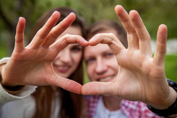 A loving couple in a good mood in the park, shows a heart from the fingers. Young couple in the park