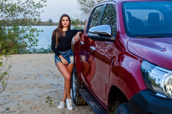 Kısa kot şortlu, uzun saçlı ve kırmızı bir kamyonetin yanında poz veren siyah elbiseli güzel seksi bir kız. Arabanın yanında poz veren kız.