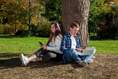Genç bir çift, dizüstü bilgisayarı, kulaklığı ve telefonu olan bir ağacın yanında otururken parkta birlikte zaman geçirir, çalışır ve çalışır. Parkta aletleri olan bir kızla birlikte olan adam.