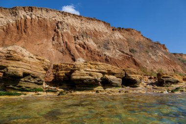 Karadeniz kıyısında çeşitli şekillerde sarı kumlu kayalar ve taşlar. Mavi gökyüzü ve turkuaz su.