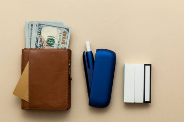 Elektronik mavi IQOS sigarası, bej arka planda parası olan kahverengi cüzdan. Metnin, logon ve tasarımın için bir fotoğraf. Dinlenme kavramı.