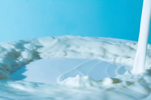 Salpicos de leite na superfície do leite sobre um fundo azul claro — Fotografia de Stock