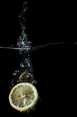Limon dilimleri suya yakın çekim, makro, sıçrama, kabarcıklar, siyah izole düşen 