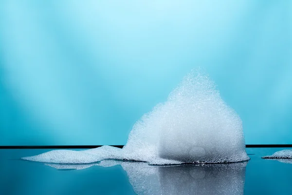 Schaumstoff, Blasen mit Reflexion auf dunklem Glas, blauer Hintergrund — Stockfoto