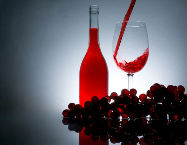 Versare il vino in un bicchiere accanto a una bottiglia di vino e uva su un tavolo con riflessione su uno sfondo vintage — Foto Stock