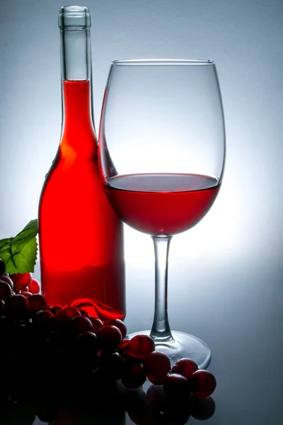 Vino in un bicchiere accanto a una bottiglia di vino e uva su un tavolo con riflessione su uno sfondo vintage — Foto Stock