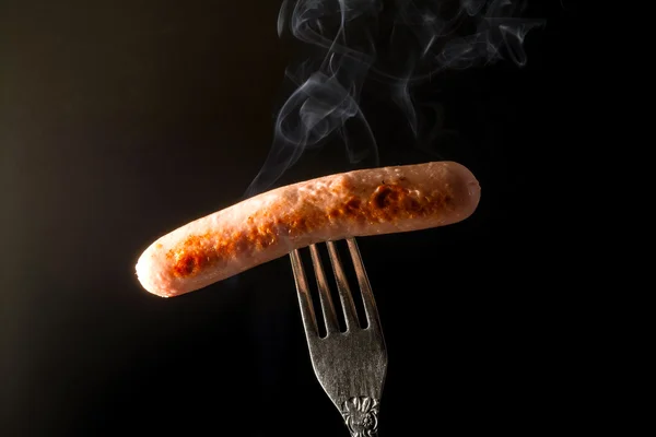 Grilled sausage on a fork with beautiful fuming smoke on dark background — Stock Photo, Image