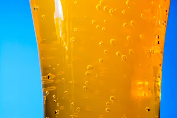 Bubbels van oranje soda in grote glazen macro op blauwe achtergrond — Stockfoto