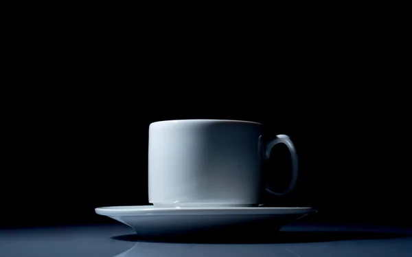 Белая чашка на серебряной тарелке крупным планом на чёрном фоне — стоковое фото