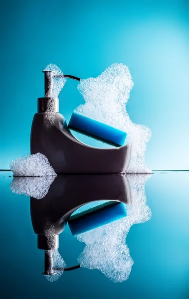 Banho minúsculo com uma esponja e espuma com reflexão sobre um fundo azul, detergente — Fotografia de Stock