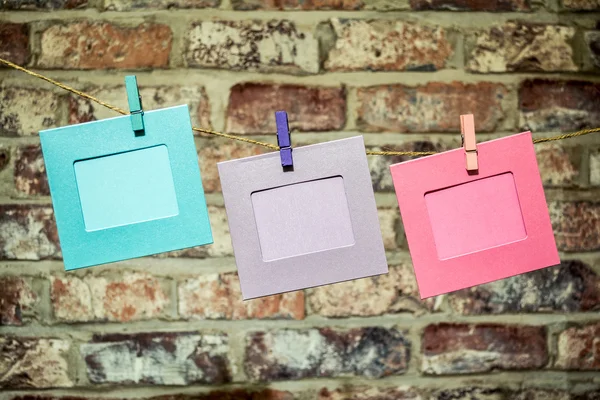 Colorful funny picture frames hanging on a rope with clothespins twine on the old, vintage brick wall background