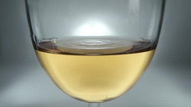 Kadehteki beyaz şarap ve düşen şarap damlalarının yaratıcı makro yavaş çekim ham videosu. Yavaşça düşen şarap damlaları olan bir bardak..