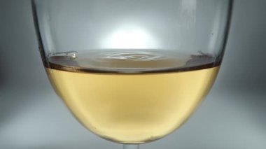 Kadehteki beyaz şarap ve düşen şarap damlalarının yaratıcı makro yavaş çekim ham videosu. Yavaşça düşen şarap damlaları olan bir bardak..