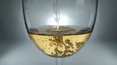 Bir bardağa dökülen beyaz şarabın yaratıcı makro yavaş çekim ham videosu. Doldurulmuş beyaz şaraplı bardaklar. Su ve kabarcıklarla yakın plan..