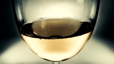 Yaratıcı makro yavaş çekim videosu beyaz şarabın bir bardaktan diğerine dalgalar gibi sıçraması. Yakın plan şarap sıçratan bir bardak. Eski grunge tarzı hoş, hafif yumuşak soluk.