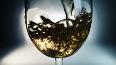 Beyaz şarabın renkli arkaplana döküldüğü yaratıcı makro yavaş çekim videosu. Doldurulmuş beyaz şaraplı bardaklar. Su ve kabarcıklarla yakın plan..