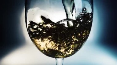 Beyaz şarabın renkli arkaplana döküldüğü yaratıcı makro yavaş çekim videosu. Doldurulmuş beyaz şaraplı bardaklar. Su ve kabarcıklarla yakın plan..