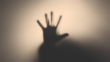 Yarı saydam bir bardağın arkasında bir adamın elinin silüeti. Öteki dünya kavramı, şiddet kurbanları, paranormal, hayaletler..