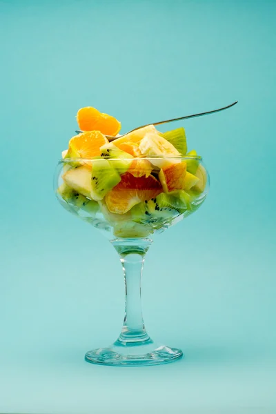 Frutta a fette in un bel bicchiere con cucchiaio da dessert su sfondo blu — Foto Stock