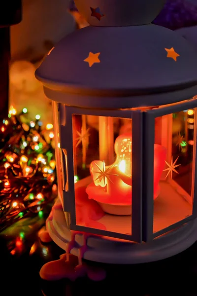 Christmas lantern with wax running down with burning candle on the background of multicolored garlands Stok Fotoğraf