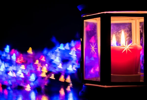 Lantern with burning candle on the right side on the background of colorful bokeh in the form of Christmas trees — Stok fotoğraf