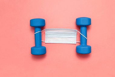Mavi halterler pembe arka planda, tıbbi maskeli.