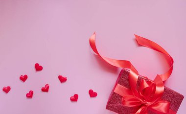 Kırmızı kurdeleli kırmızı hediye kutusu ve Sevgililer Günü için pembe arka planda kalpler. Metin için boşluk.