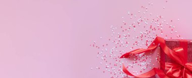 Kırmızı kurdeleli kırmızı hediye kutusu ve Sevgililer Günü için pembe arka planda kalpler. Mesaj için yer var. Uzun bayrak.