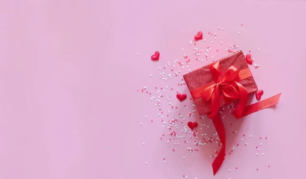 Caja roja de regalo con lazo rojo y corazones sobre fondo rosa para el día de San Valentín. Espacio para el texto. Banner ancho largo. — Foto de Stock