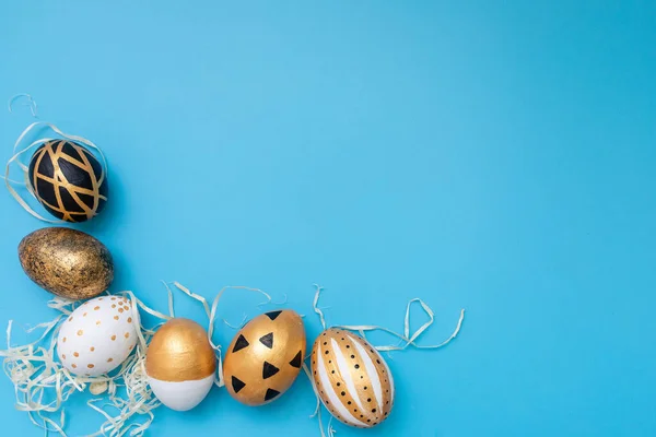 Huevos de Pascua dorados, negros y blancos sobre fondo azul. Geometría. Mínimo concepto de Pascua. Vista desde arriba. Tarjeta de Pascua con espacio de copia para texto. — Foto de Stock