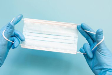 Doctor hand wear blue medical gloves holds antivirus face mask on blue background for pandemic, airborne diseases, outbreak, Covid19 concept. Copy spece.