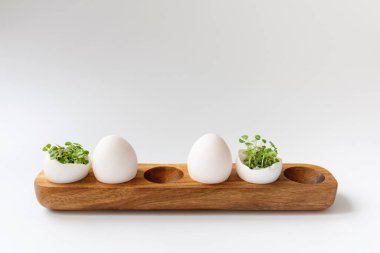 Beyaz arka planda, tahta yumurta kutusunda beyaz yumurta içinde yeşil lahanalar. Seçici odak, uzayı kopyala. Eko konsepti. Paskalya Asgari Konsepti.