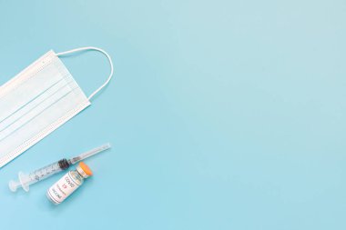 Koruyucu tıbbi maske, şırınga ve mavi arka planda kovan 19 aşısı. Aşılama, aşılama, insanların Covid 'den korunması..