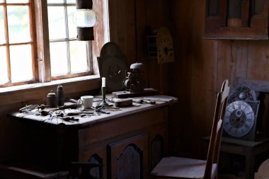 Saat imalatçıları atölyesi. Masanın üzerine doğal güneş ışığı parçaları ve aletler serpiştirilmiş..