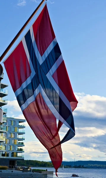 Official Norwegian national flag waving in the wind with blue skies in the background.