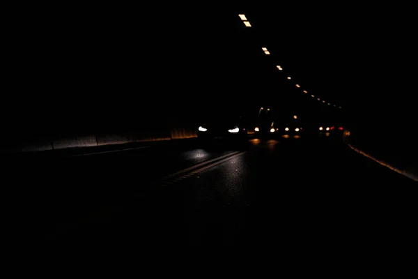 汽车在只有前灯和隧道照明显示的黑暗隧道内行驶 高质量的照片 — 图库照片