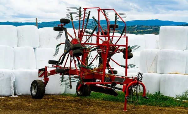 背景に白いプラスチックで包まれた草の干し草のベールのシラージュと赤いローター熊手農業機械 そうだ 高品質の写真 — ストック写真