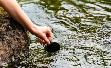Yürüyüşçülerin bardak katladıkları ellerle bardağı doldurmak için akarsu yüzeyine uzanırlar. - Evet. Yüksek kalite fotoğraf