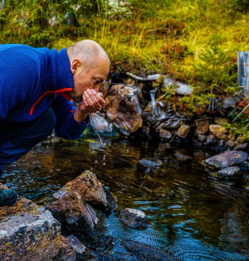 Yürüyüşçü küçük bir dereden temiz buzul suyu içiyor. Kapat.. 
