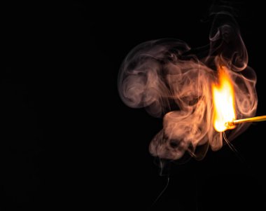 Siyah arka planda izole edilmiş, etrafı dumanla çevrili tek bir kibrit yanıyor. Yüksek kalite fotoğraf