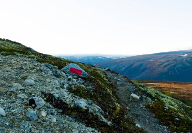 Dağların arasından geçen yolu gösteren parlak kırmızı işaretli bir kaya. Norveç Turizm Birliği DNT tarafından kurulmuştur. - Evet. Yüksek kalite fotoğraf