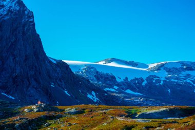 Dağlarda karlı tepeleri, mavi gökyüzü ve sonbahar renkleri olan bir vadide küçük ahşap bir kulübe. - Evet. Yüksek kalite fotoğraf