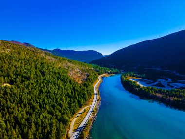 Dağlardaki bir nehir vadisinde uzanan otoban temiz, berrak bir mavi su ve vadinin gölgesinde donmuş düzlüklerle dolu. - Evet. Yüksek kalite fotoğraf