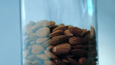 Klasik cam bir kavanozda depolanmış lezzetli ham bademler yavaşça dönüyor, beyaz arkaplanda izole edilmiş bir video.. 