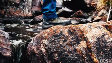 Yürüyüşçü kayaların üzerinde yürüyerek dereyi geçiyor, çizme ve bacak manzarası..