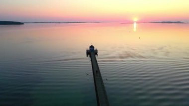 Gün batımında deniz kenarındaki uzun ahşap iskele, üzerinden uç..